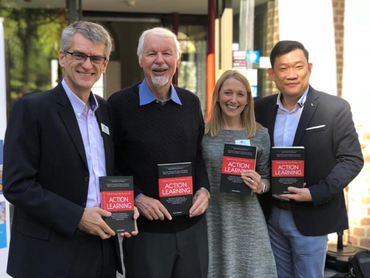 The four co-authors of Optimizing the Power of Action Learning, third edition, each holding a copy of the book